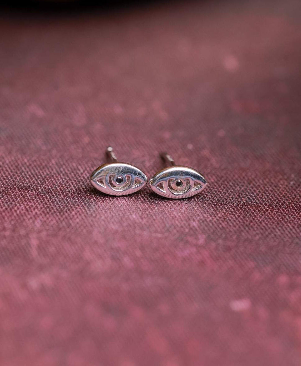 Silver eye-shaped earrings on a textured red surface