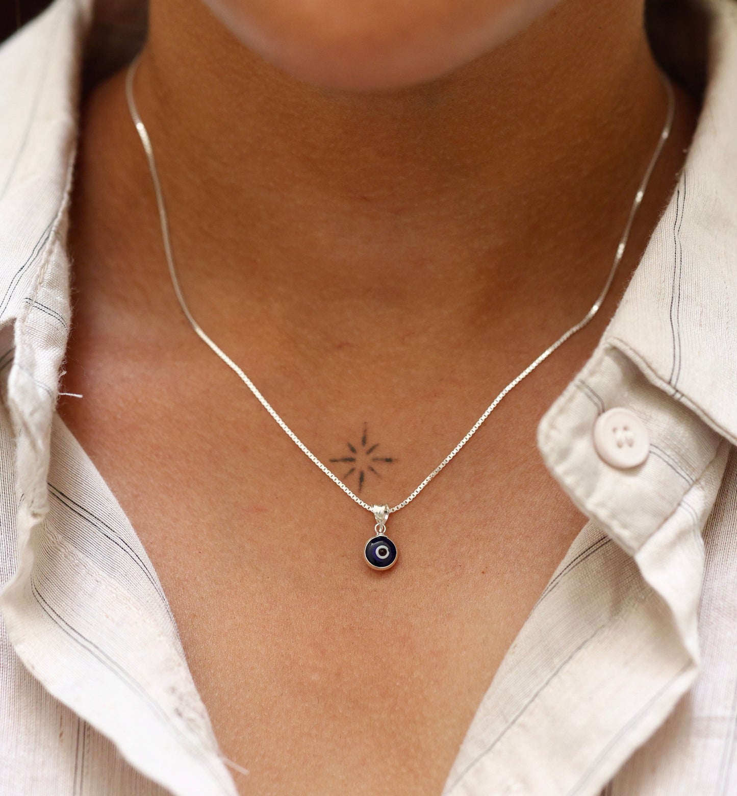 Woman wearing a minimalist 92.5 sterling silver necklace with a small blue evil eye pendant for protection.