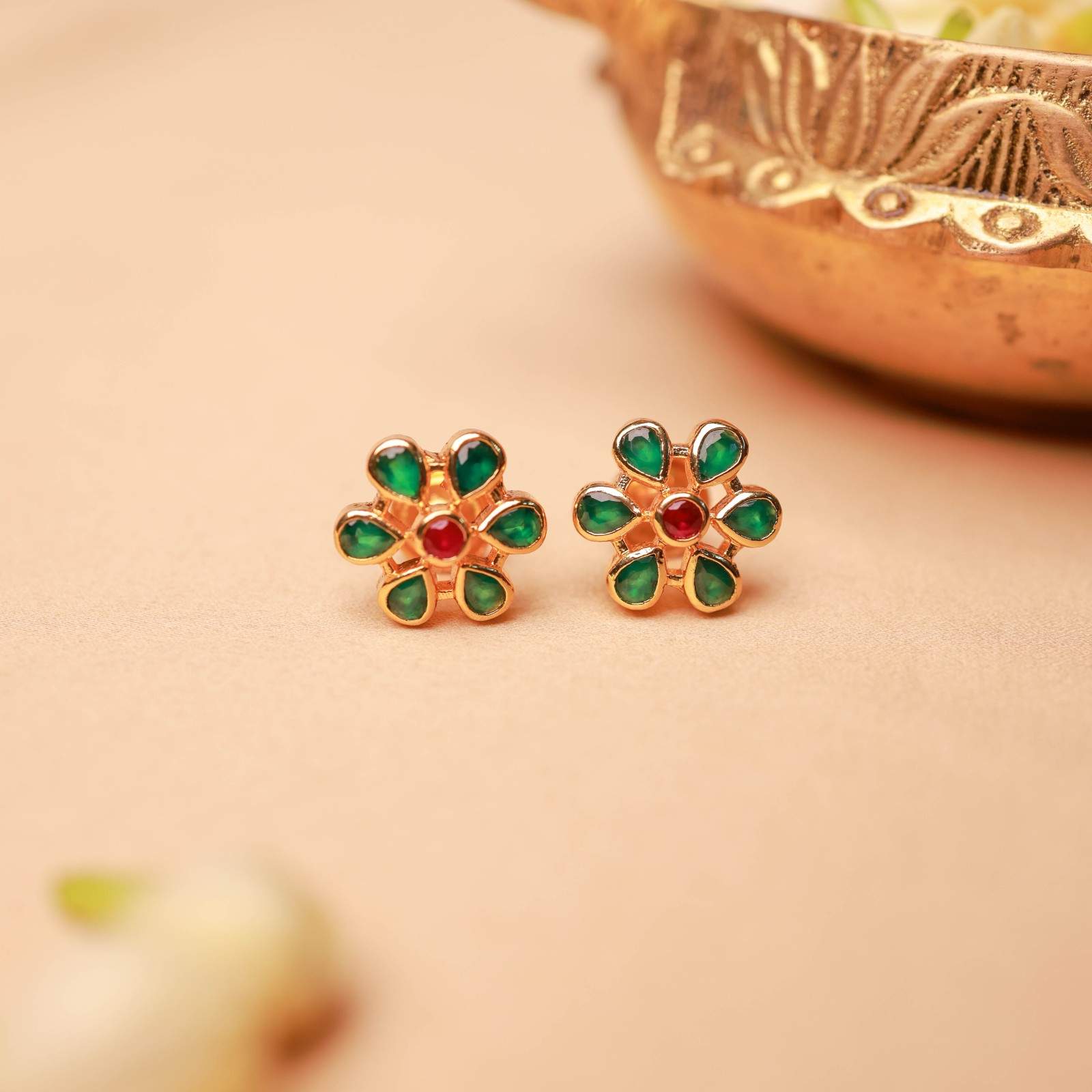 Gold earrings with green and red stones on a beige background