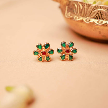 Gold earrings with green and red stones on a beige background