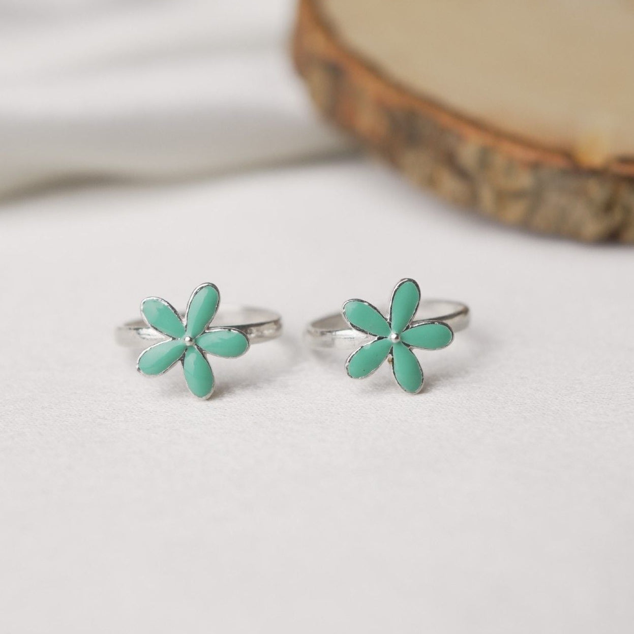 Pair of turquoise flower-shaped earrings on a white surface with a wooden slice in the background.