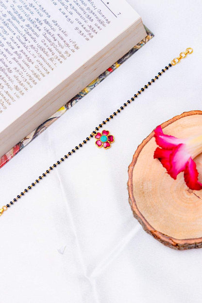 Mangalsutra bracelet with black beads and a pink–turquoise stone flower charms.