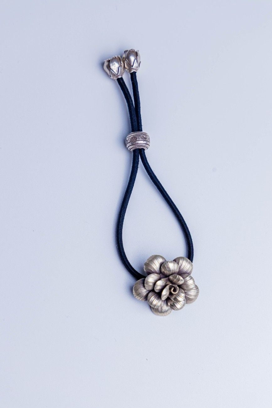 Handcrafted sterling silver floral accessory with adjustable black cord, used as both hairband and bracelet.