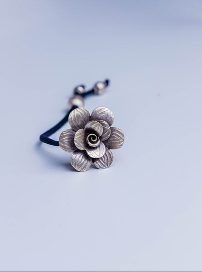 Handcrafted sterling silver floral accessory with adjustable black cord, used as both hairband and bracelet.