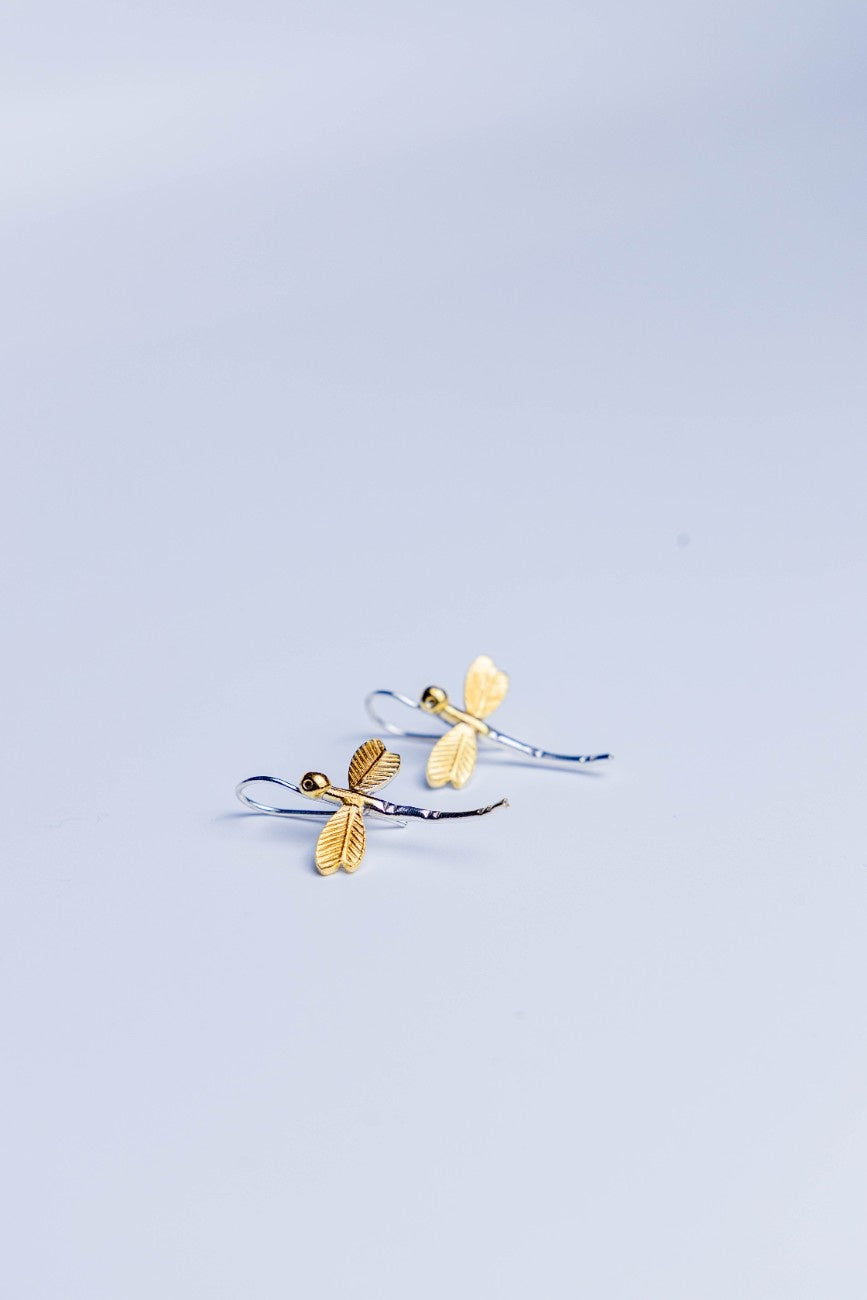 Dual-tone dragonfly earrings with golden wings and silver body placed.