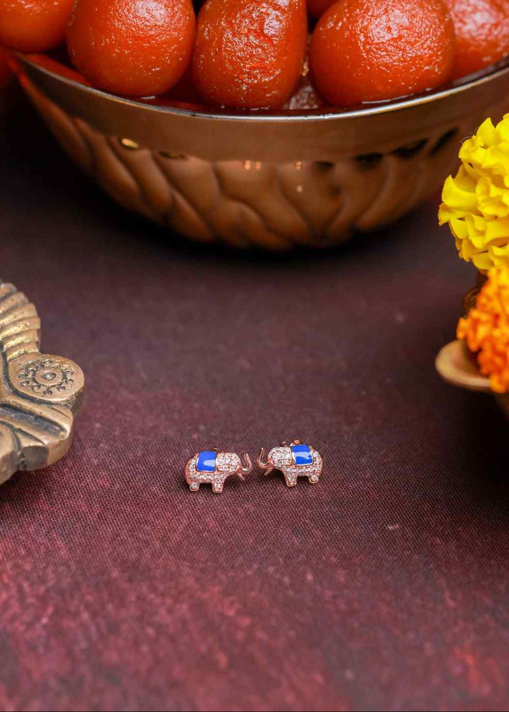 Small elephant-shaped earrings with blue gemstones on a dark fabric background.