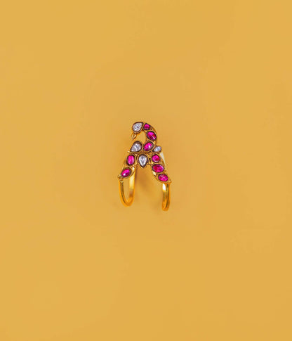 A gold-plated split ring featuring a decorative top with pink teardrop-shaped stones, a white teardrop stone, and a small round clear stone, set against a solid mustard yellow background.