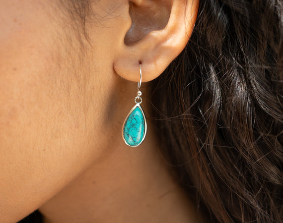 "Close-up of a woman wearing a teardrop-shaped turquoise gemstone earring with silver hook setting"