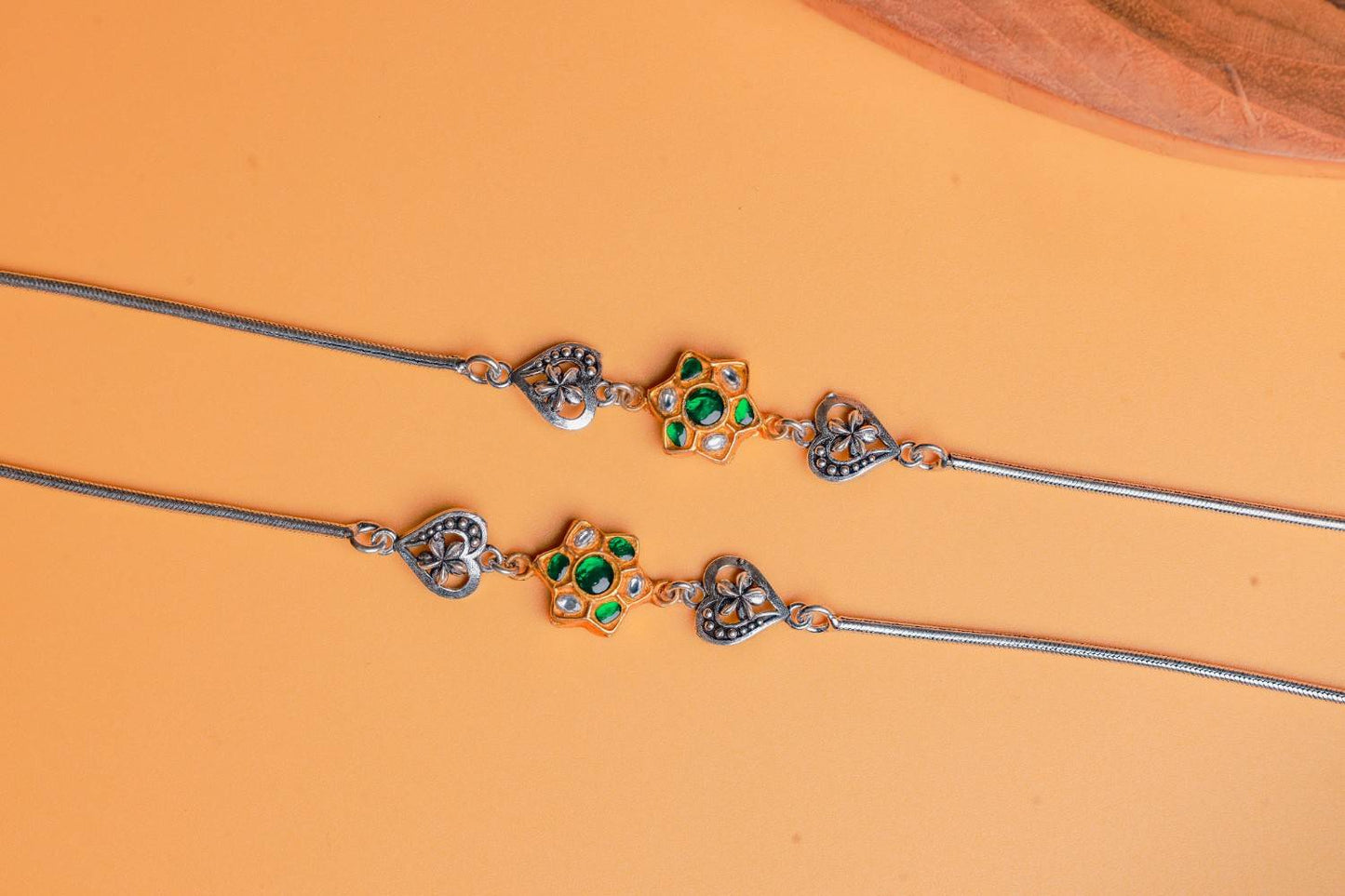 Dual-tone silver anklets with green Kundan floral motifs and oxidized heart charms by Sil’alankaraa.