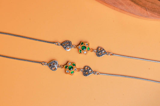 Dual-tone silver anklets with green Kundan floral motifs and oxidized heart charms by Sil’alankaraa.