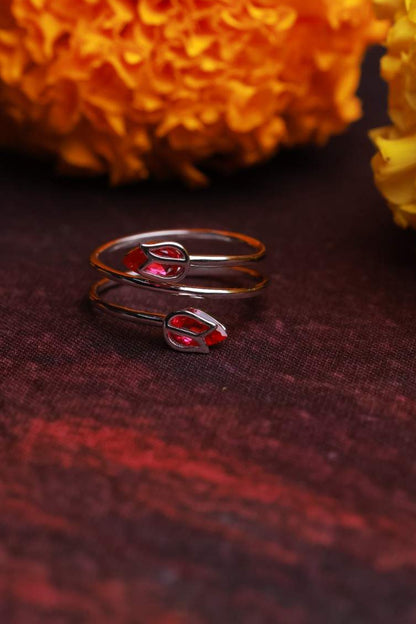 Silver ring with red stones on a dark surface with yellow flowers in the background
