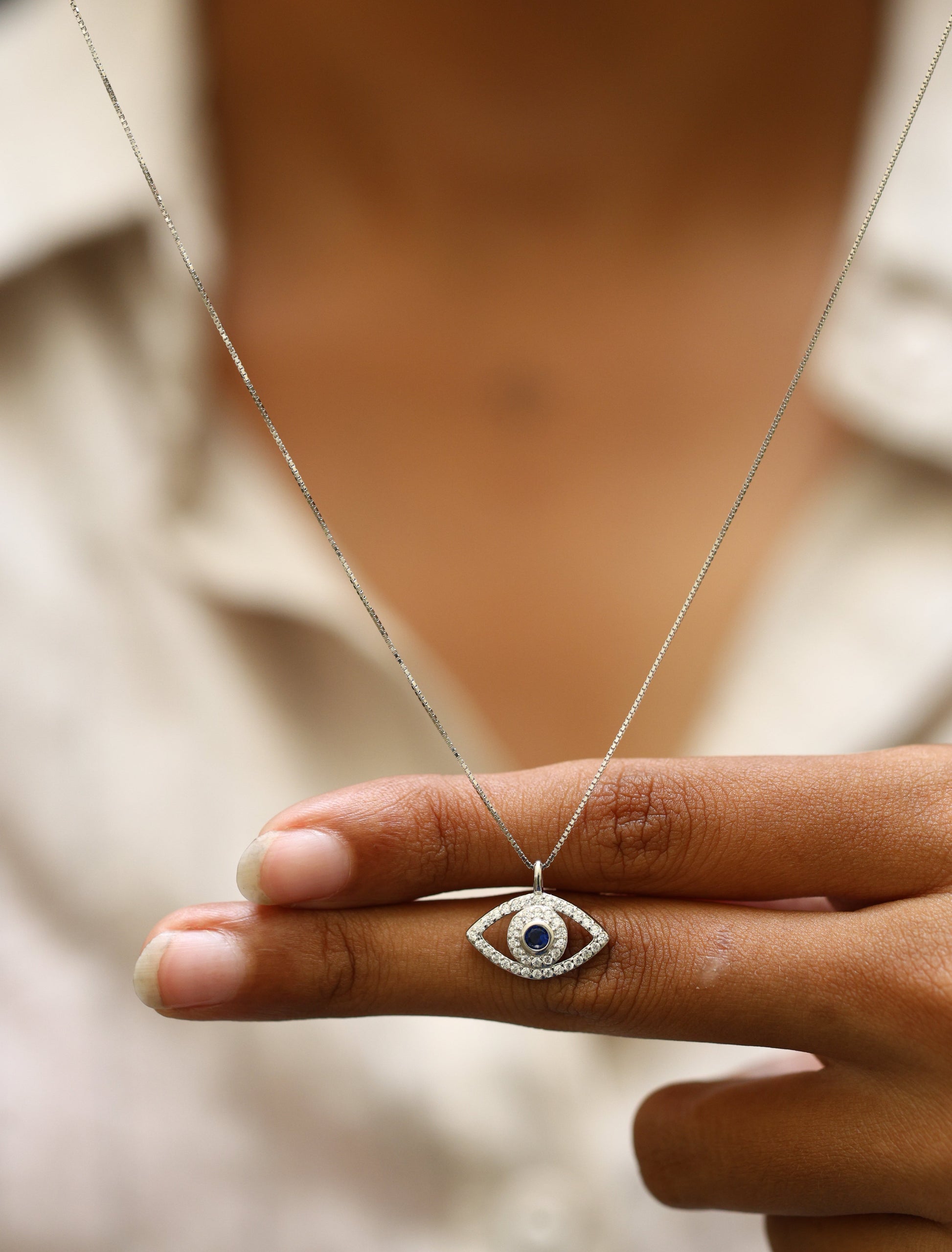 Close-up of 92.5 sterling silver evil eye pendant necklace with cubic zirconia and blue center stone, held by hand.