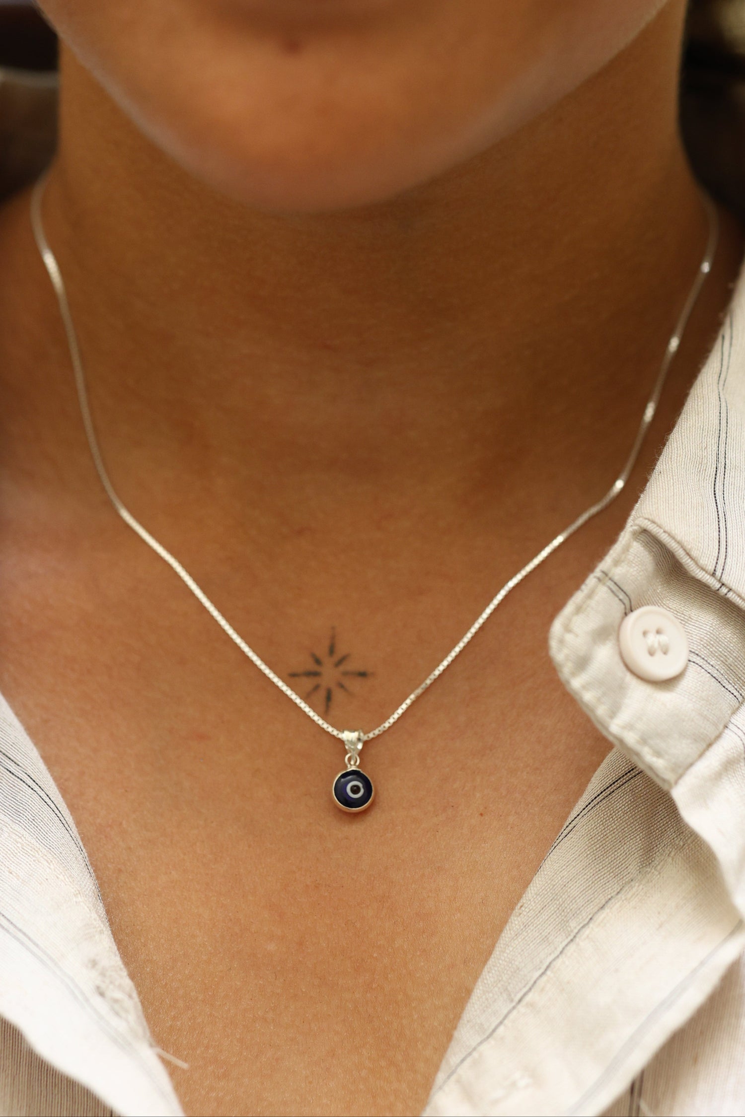 Woman wearing a minimalist 92.5 sterling silver necklace with a small blue evil eye pendant for protection.