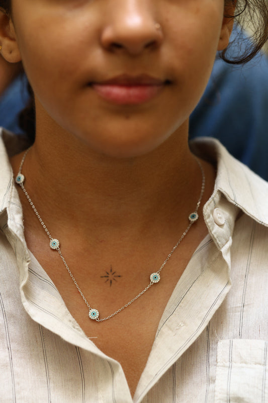 Woman wearing a 92.5 sterling silver chain necklace with multiple blue enamel evil eye charms for protection and style.