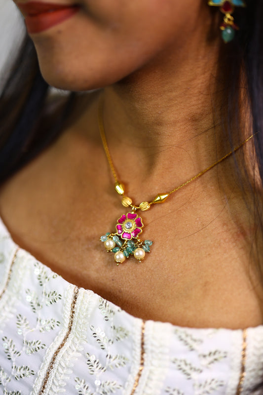Close-up of a woman wearing a floral gold-plated necklace with pearl drops and colored stones.
