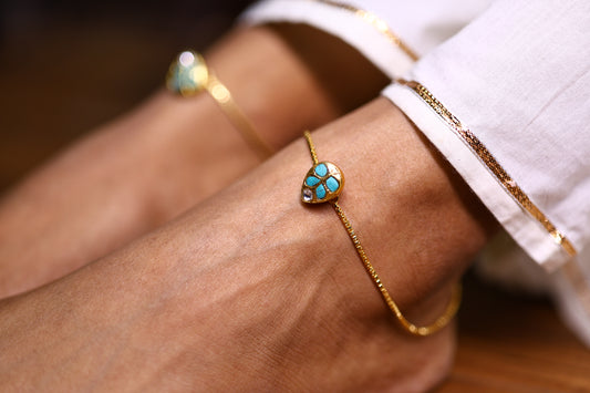 Close up of a gold-plated anklet with a turquoise stone on a woman's anklet
