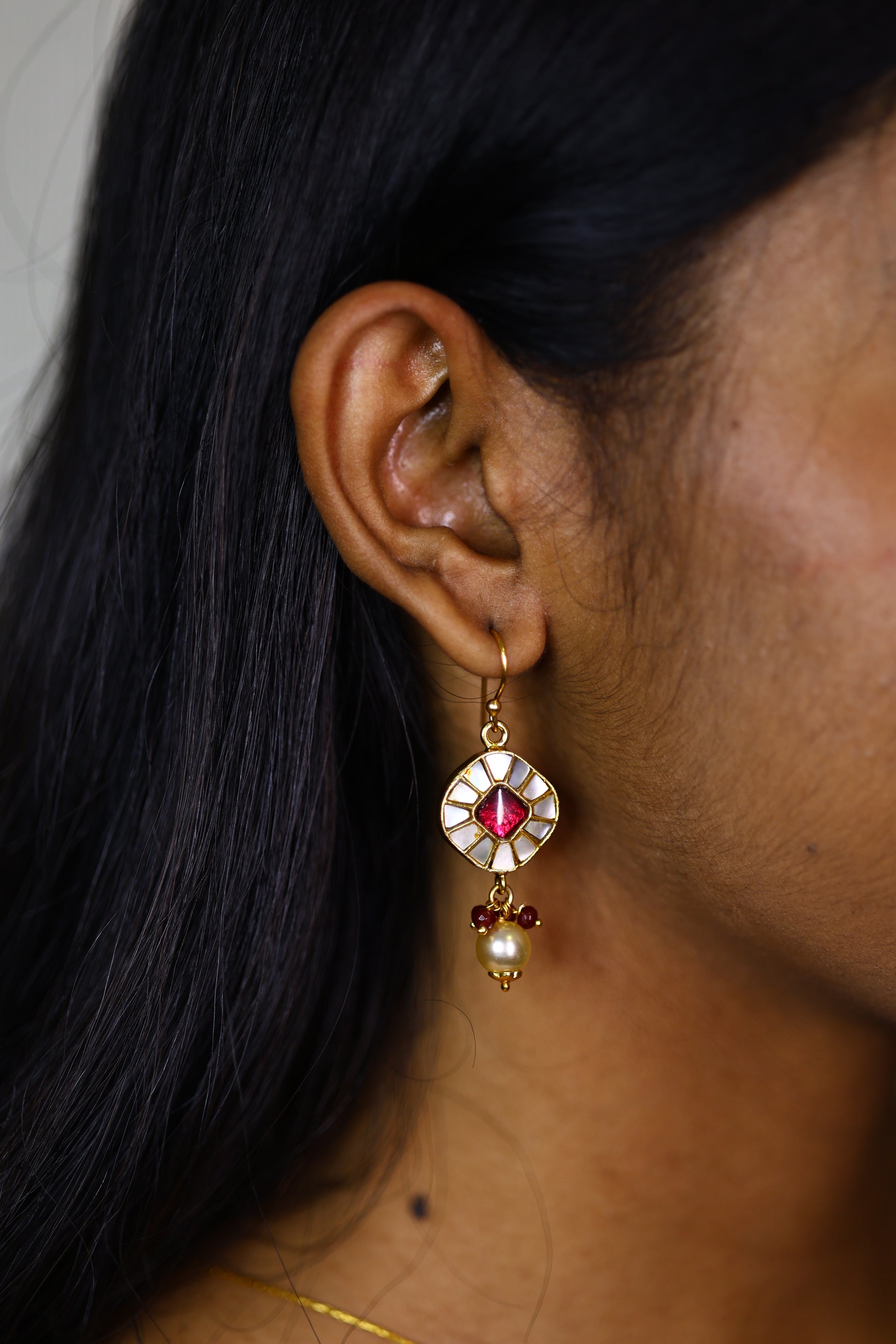 Close-up of a traditional Indian Kundan drop earring with a red gemstone and pearl 
