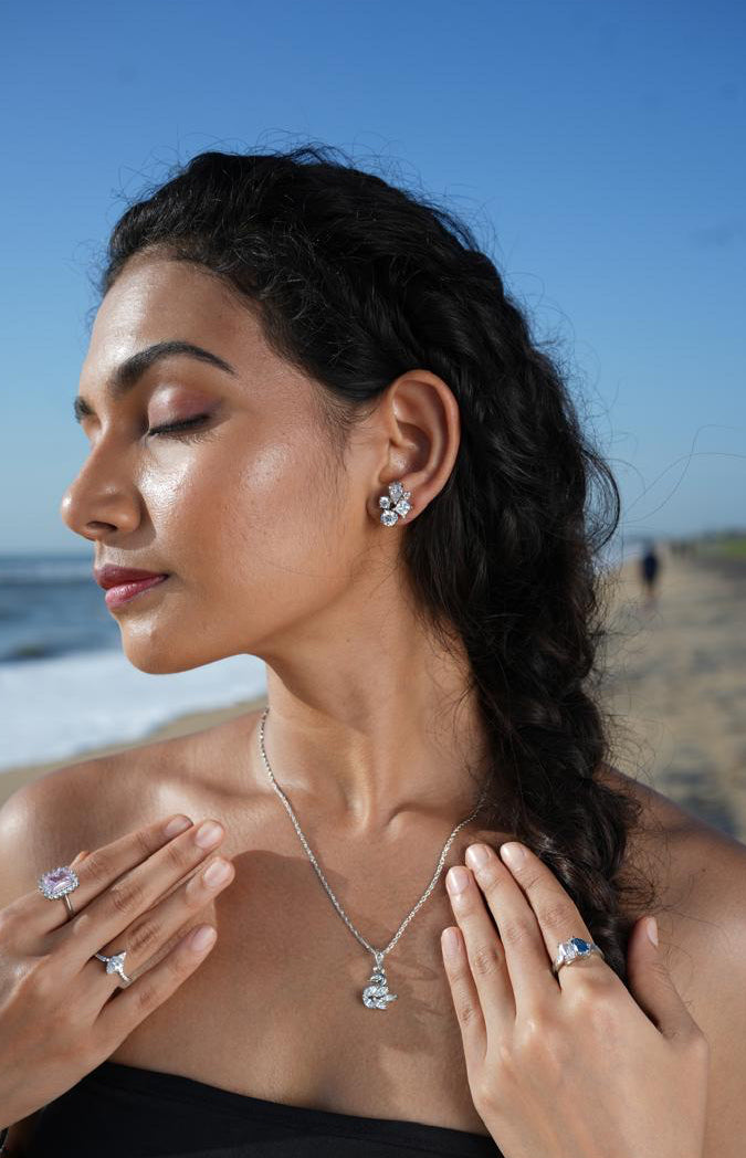 Woman on a beach wearing jewelry, with a clear blue sky and ocean in the background.