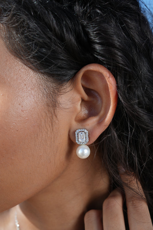 Close-up of a woman wearing 92.5 sterling silver earrings with zircon stones and a pearl drop.
