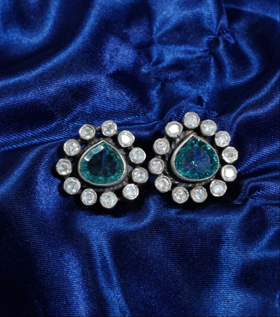 Pair of earrings with green gemstones and clear stones on a blue satin background
