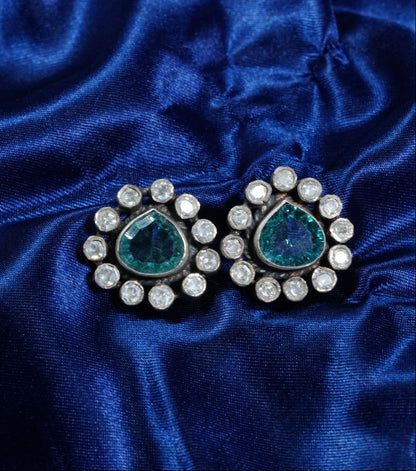 Pair of earrings with green gemstones and clear stones on a blue satin background